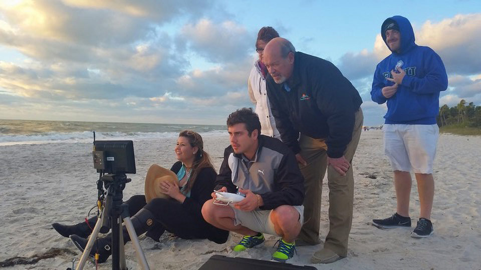 Five people on the beach operate a drone