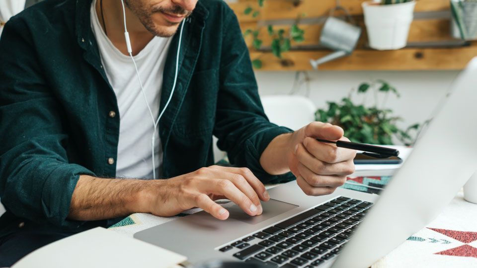 man on computer in green shirt holding pencil wearing headphones